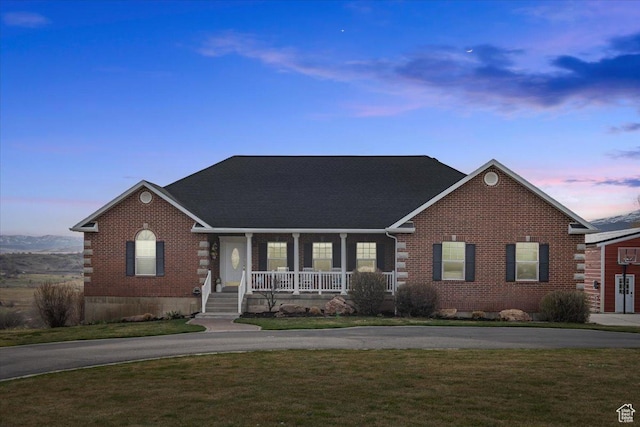 view of front of property with curved driveway, covered porch, a front yard, and brick siding