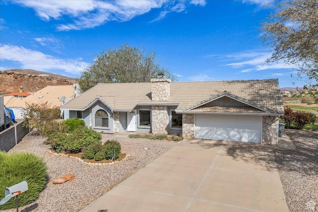 view of front facade featuring stone siding, a tile roof, an attached garage, a chimney, and driveway