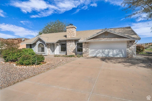 ranch-style home with stone siding, a tile roof, an attached garage, a chimney, and concrete driveway