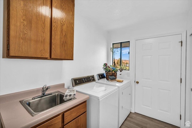 laundry area featuring wood finished floors, washing machine and dryer, a sink, and cabinet space