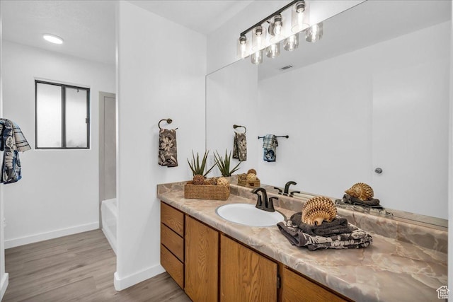 bathroom featuring a bathing tub, vanity, baseboards, and wood finished floors