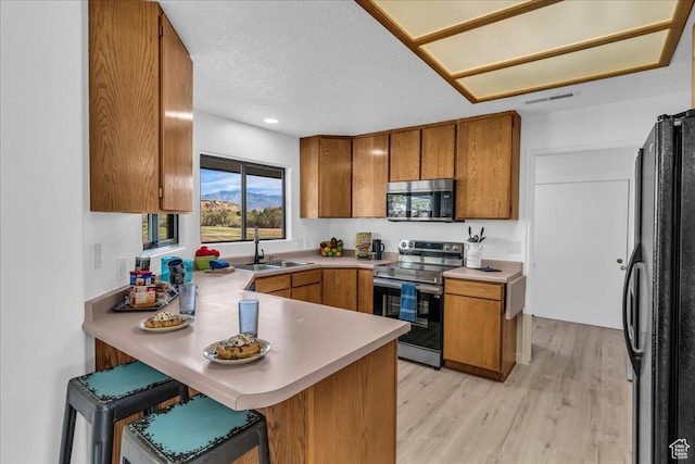 kitchen with a peninsula, brown cabinets, a sink, and appliances with stainless steel finishes