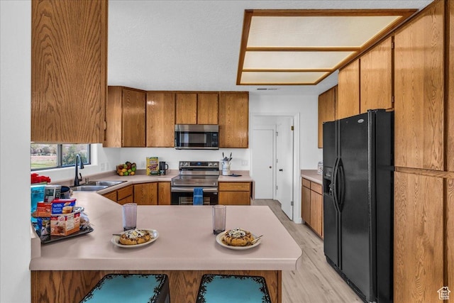 kitchen featuring brown cabinets, appliances with stainless steel finishes, a peninsula, and a sink
