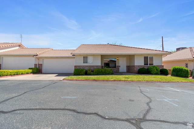 single story home featuring brick siding, a tiled roof, a garage, and concrete driveway