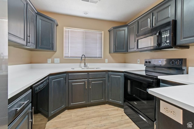 kitchen with a sink, light countertops, black appliances, and light wood-style floors