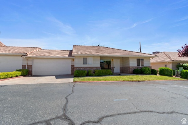 single story home featuring concrete driveway, a front lawn, brick siding, a garage, and a tiled roof