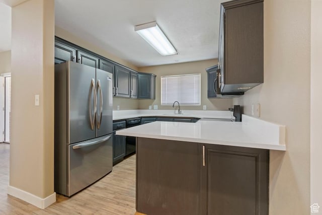 kitchen with light wood-style floors, freestanding refrigerator, stove, a peninsula, and light countertops