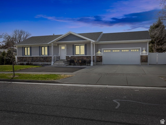 ranch-style home featuring driveway, stone siding, fence, and an attached garage