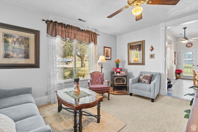 carpeted living room with ceiling fan, visible vents, and a wood stove