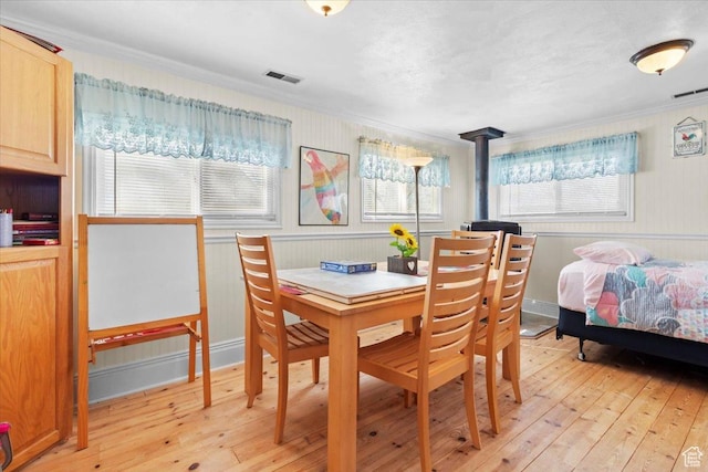 dining space featuring a wood stove, light wood-style flooring, visible vents, and ornamental molding