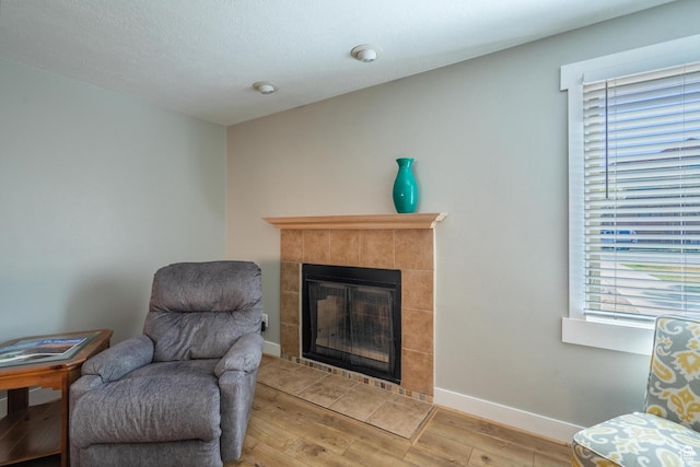 living area with baseboards, wood finished floors, and a tiled fireplace