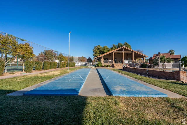 surrounding community with a lawn, fence, and shuffleboard