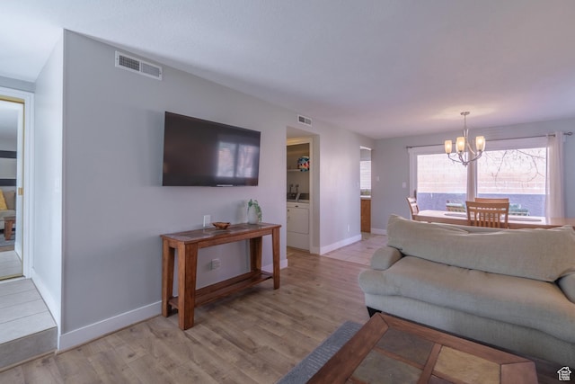 living area featuring a chandelier, light wood-style floors, visible vents, and baseboards