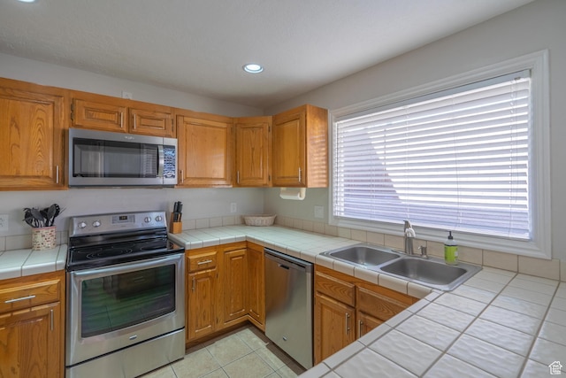 kitchen with recessed lighting, tile countertops, light tile patterned floors, a sink, and appliances with stainless steel finishes