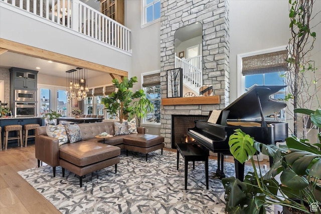 living room with a stone fireplace, a wealth of natural light, a towering ceiling, and wood finished floors