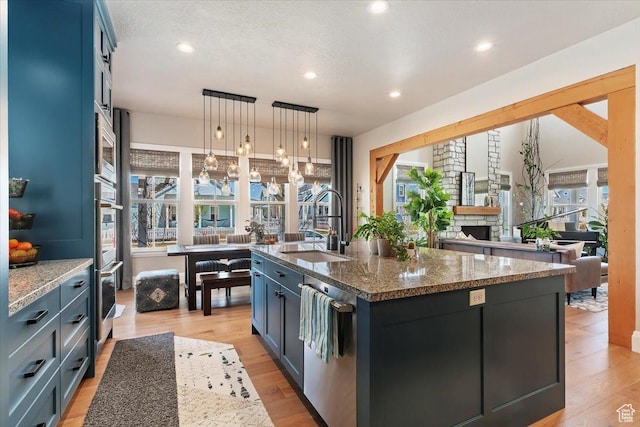 kitchen featuring dark stone counters, light wood finished floors, a sink, and a stone fireplace