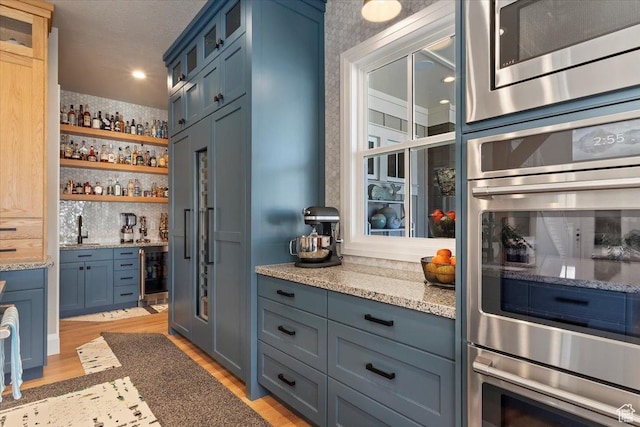 bar with light wood-style flooring, wallpapered walls, wet bar, and stainless steel appliances