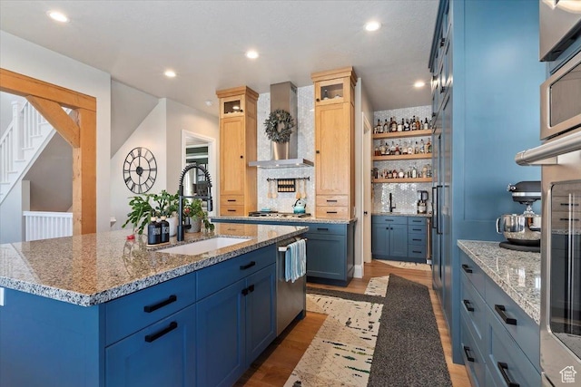 kitchen with a sink, light wood finished floors, wall chimney exhaust hood, and blue cabinets