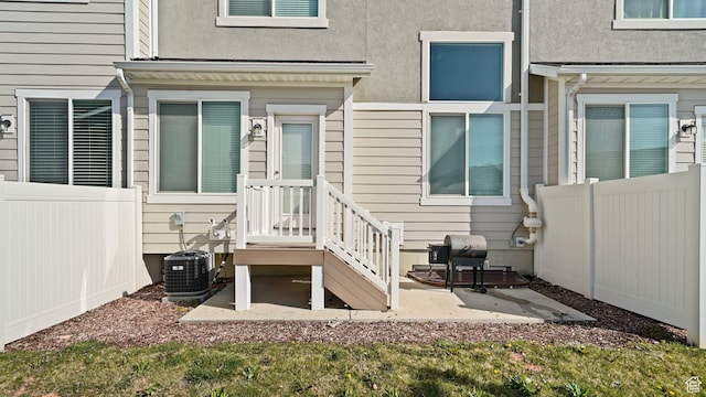 doorway to property with central AC, fence, a patio, and stucco siding