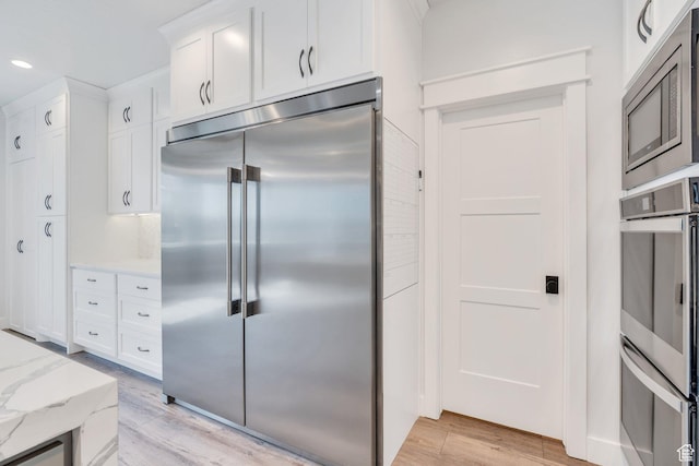 kitchen featuring built in appliances, white cabinetry, recessed lighting, light wood finished floors, and light stone counters