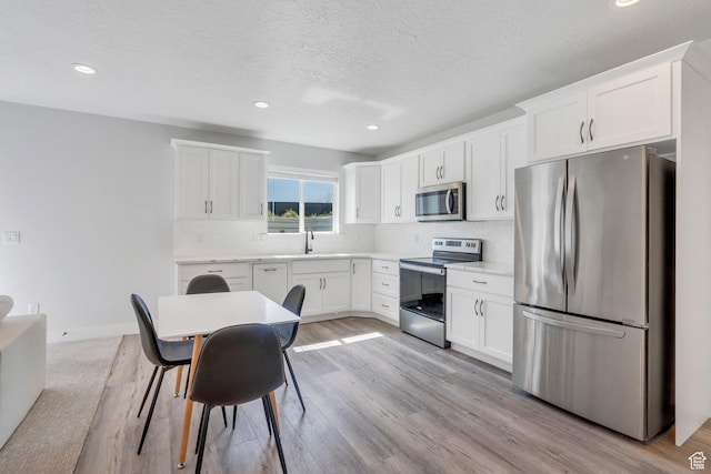 kitchen with tasteful backsplash, light wood-type flooring, white cabinetry, appliances with stainless steel finishes, and a sink