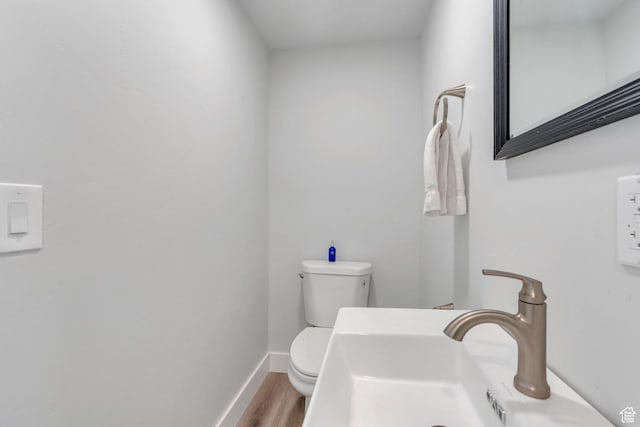 bathroom with a sink, toilet, wood finished floors, and baseboards