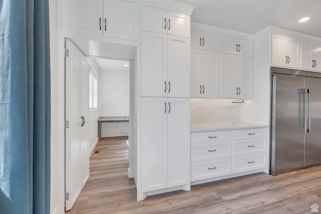 kitchen with built in refrigerator, light stone counters, recessed lighting, light wood-style flooring, and white cabinetry