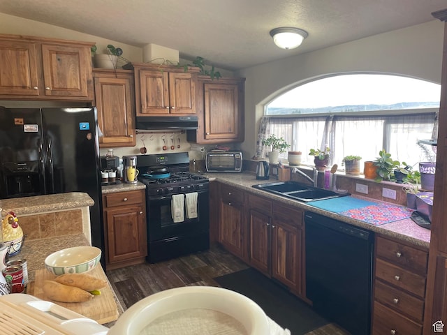 kitchen featuring vaulted ceiling, under cabinet range hood, a sink, and black appliances