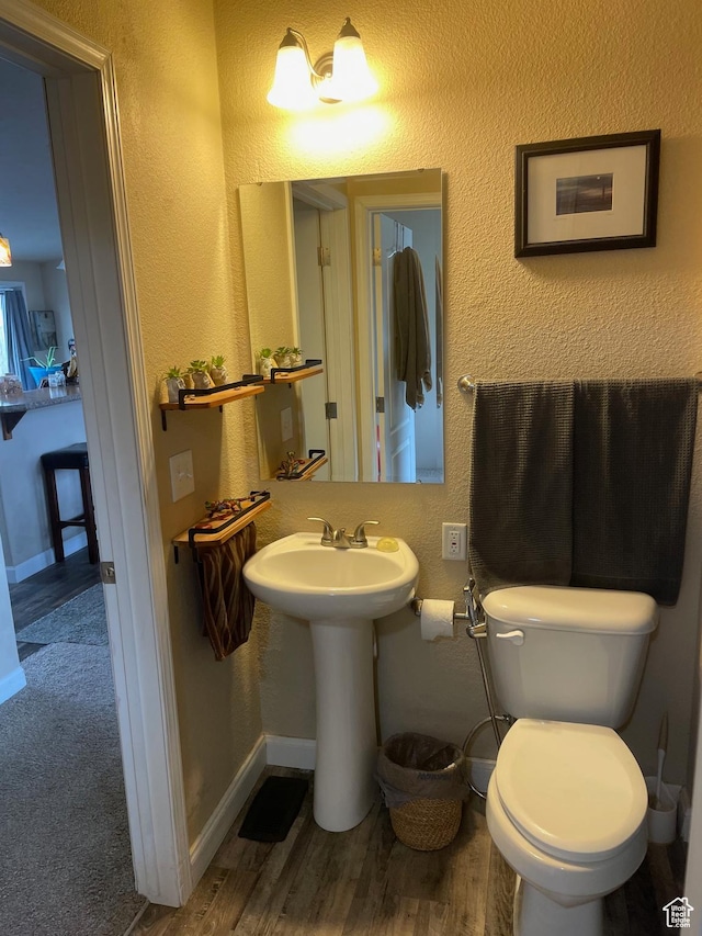 half bath featuring a textured wall, toilet, wood finished floors, and a sink