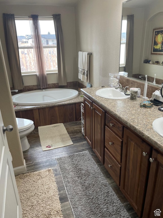 bathroom with double vanity, wood finished floors, toilet, a sink, and a garden tub