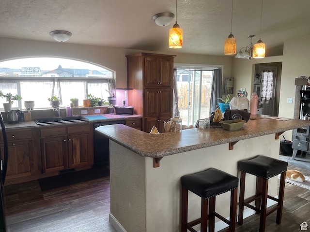 kitchen with a sink, dishwasher, a wealth of natural light, a kitchen bar, and dark wood-type flooring