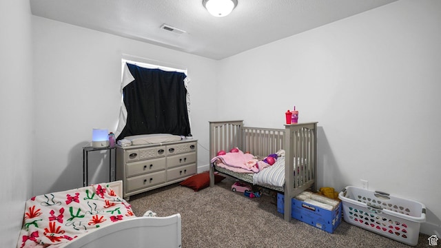 bedroom with a textured ceiling, carpet flooring, visible vents, and a crib