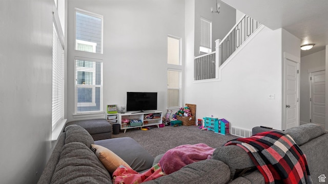 carpeted living area with stairs, a towering ceiling, and visible vents