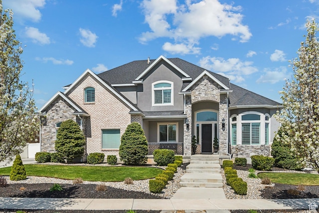 view of front of property featuring roof with shingles, stucco siding, stone siding, and a front lawn