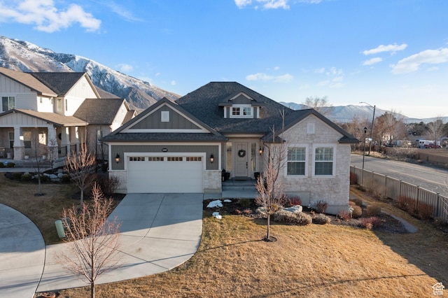 view of front facade with concrete driveway, a mountain view, stone siding, a garage, and fence