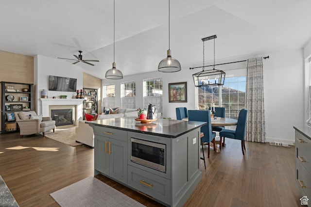 kitchen with stainless steel microwave, dark countertops, dark wood-style floors, and gray cabinets
