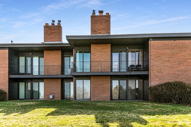 back of house featuring a balcony, a chimney, brick siding, and a yard