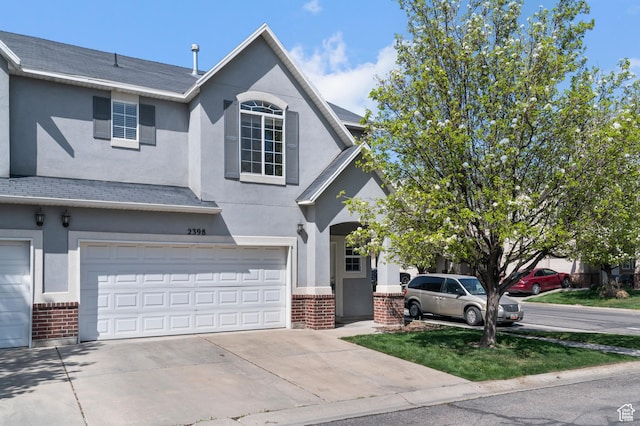 traditional home featuring concrete driveway, brick siding, stucco siding, and an attached garage