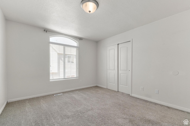 unfurnished bedroom featuring baseboards, a closet, a textured ceiling, visible vents, and carpet