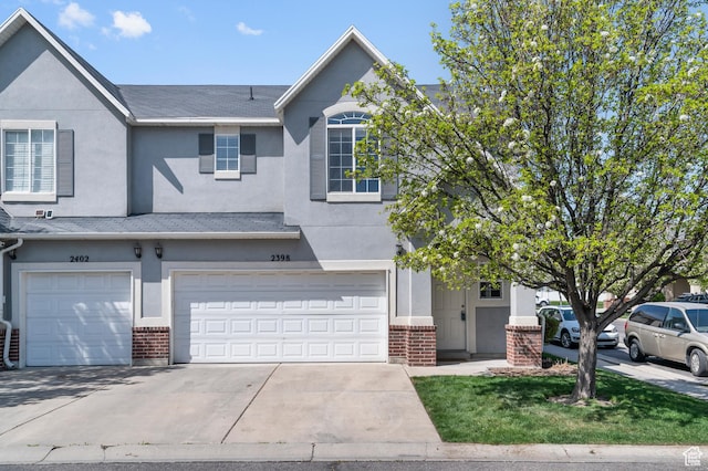 multi unit property with brick siding, an attached garage, driveway, and stucco siding