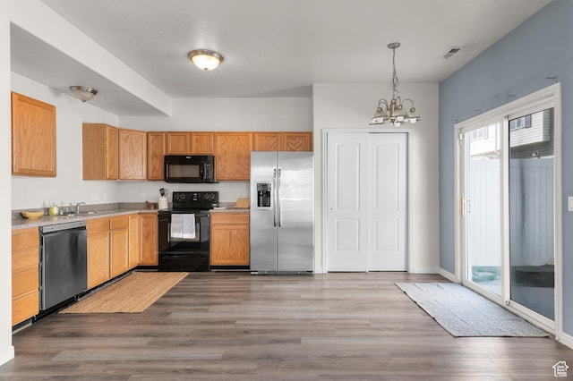 kitchen with wood finished floors, a sink, black appliances, and a notable chandelier