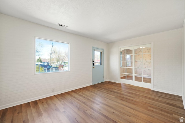 1489 W 300 S, Salt Lake City, UT 84104 - unfurnished room featuring visible vents, brick wall, wood finished floors, and a textured ceiling