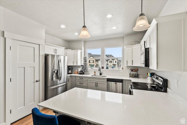 kitchen with a sink, light countertops, a peninsula, stainless steel appliances, and light wood-style flooring