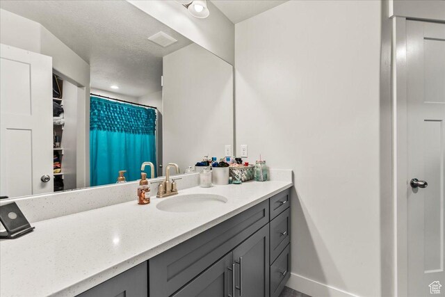 full bathroom with a textured ceiling, vanity, baseboards, and a shower with curtain