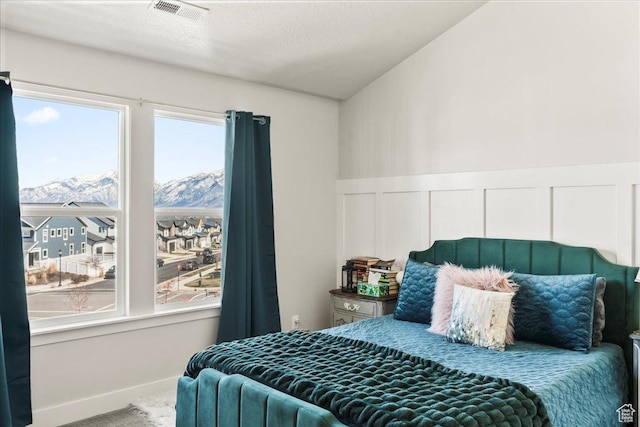 carpeted bedroom with a mountain view, visible vents, a wainscoted wall, and a textured ceiling