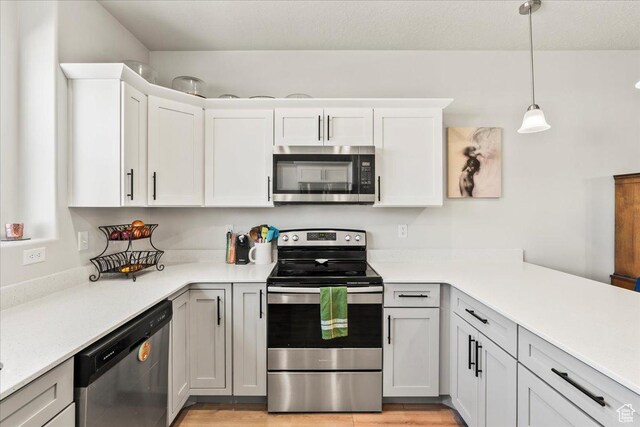 kitchen featuring light countertops, white cabinets, decorative light fixtures, appliances with stainless steel finishes, and light wood finished floors