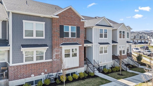 multi unit property with entry steps, board and batten siding, central air condition unit, a residential view, and roof with shingles