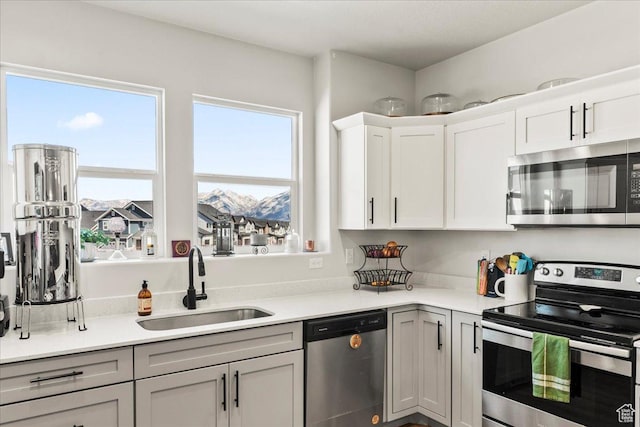 kitchen with light countertops, white cabinetry, gray cabinetry, stainless steel appliances, and a sink