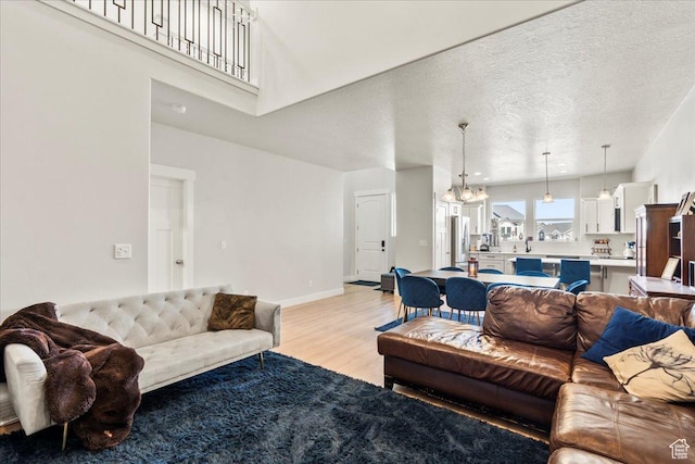 living area with light wood-style flooring, a textured ceiling, a towering ceiling, a notable chandelier, and baseboards