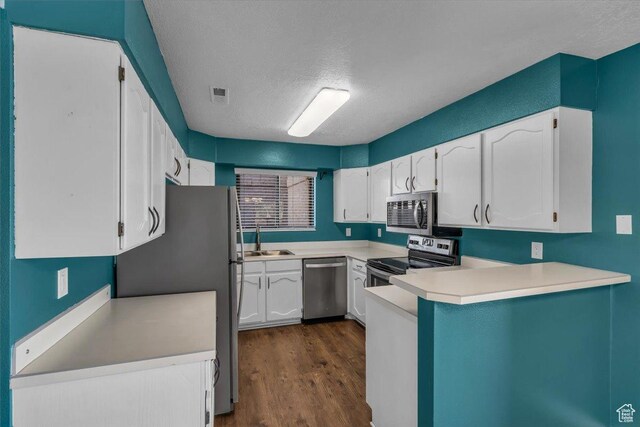 kitchen featuring a peninsula, white cabinets, appliances with stainless steel finishes, a sink, and dark wood-style floors